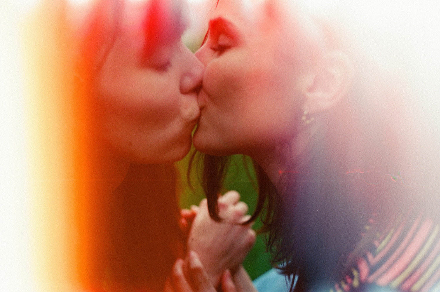 a photograph of two women kissing with reddish light flares coming in on each side